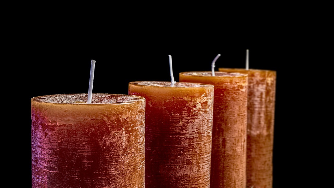 Four unlit brown pillar candles with pale upright wicks overlap against a black background.